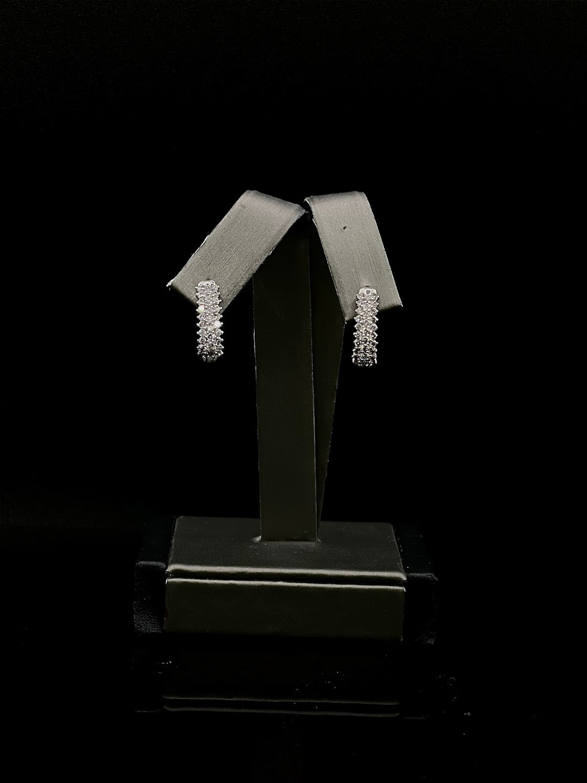 Pair of white gold diamond half hoop earrings on a black stand against a black background