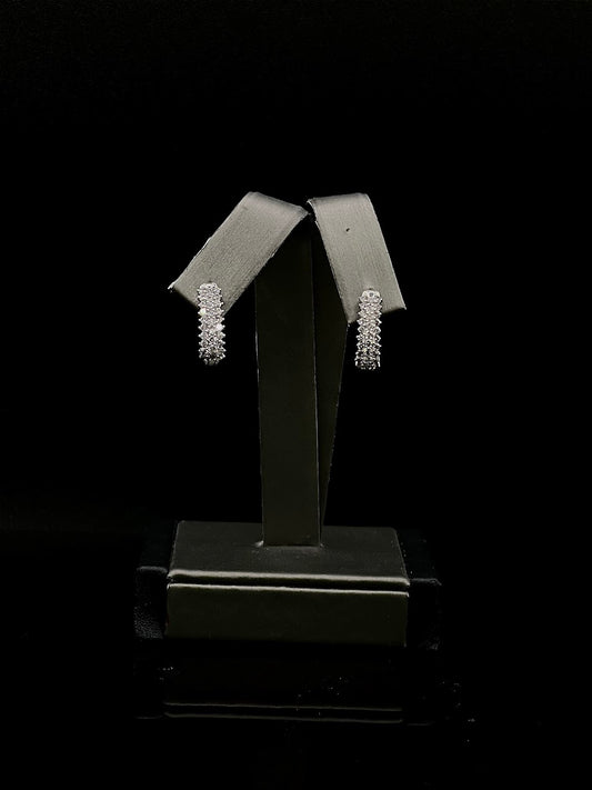 Pair of white gold diamond half hoop earrings on a black stand against a black background